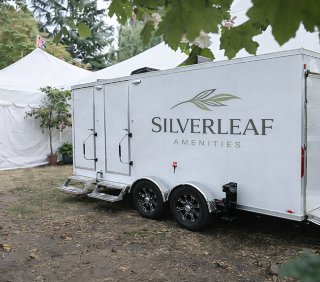 Luxury restroom trailer positioned beside large white event tents at an outdoor gathering or festival.