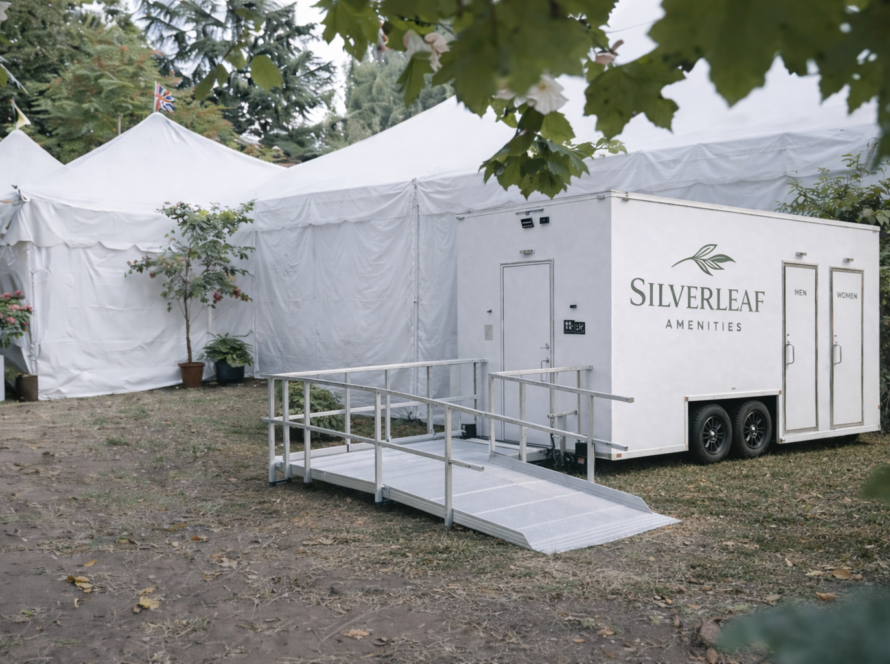 Luxury restroom trailer positioned beside large white event tents at an outdoor gathering or festival.