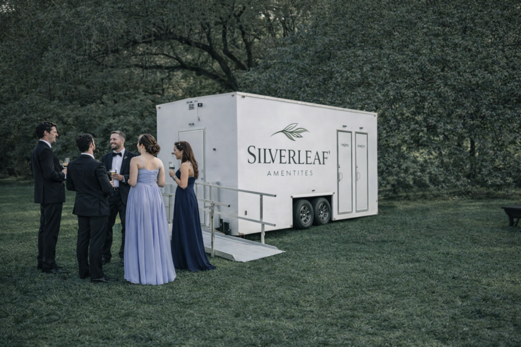 Luxury restroom trailer by Silverleaf Amenities at a wedding or outdoor event with guests standing nearby on a green lawn.