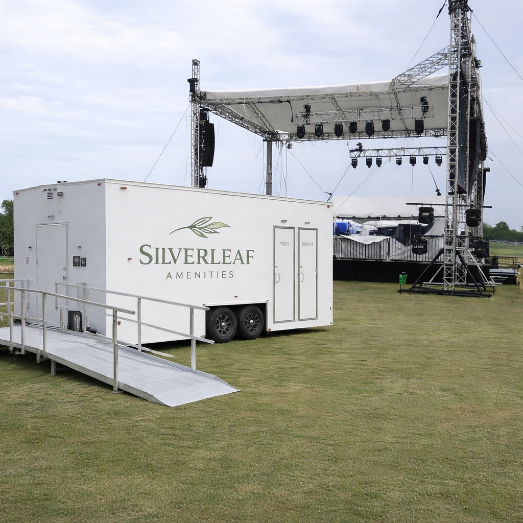 ADA-compliant restroom trailer with ramp at outdoor event near stage setup, available for festival and event rentals in Colorado
