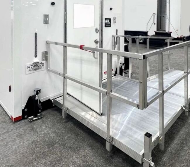 Close-up of ADA restroom trailer ramp with handrails and accessible entry door, available for event rentals in Colorado