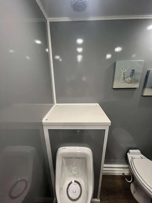 Clean modern interior of a luxury restroom trailer with urinal and toilet, available for event and construction rentals in Colorado