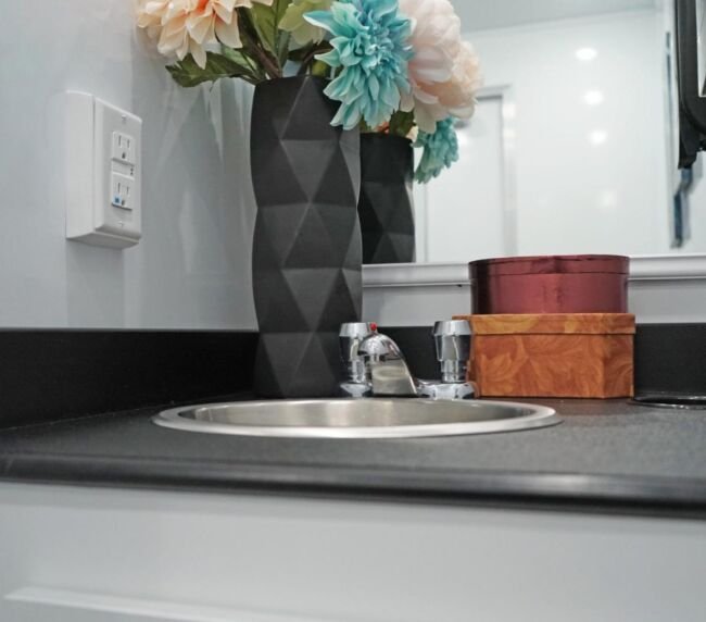 Modern sink and vanity inside a luxury restroom trailer featuring floral decor, mirror, and clean countertop for upscale event experiences.