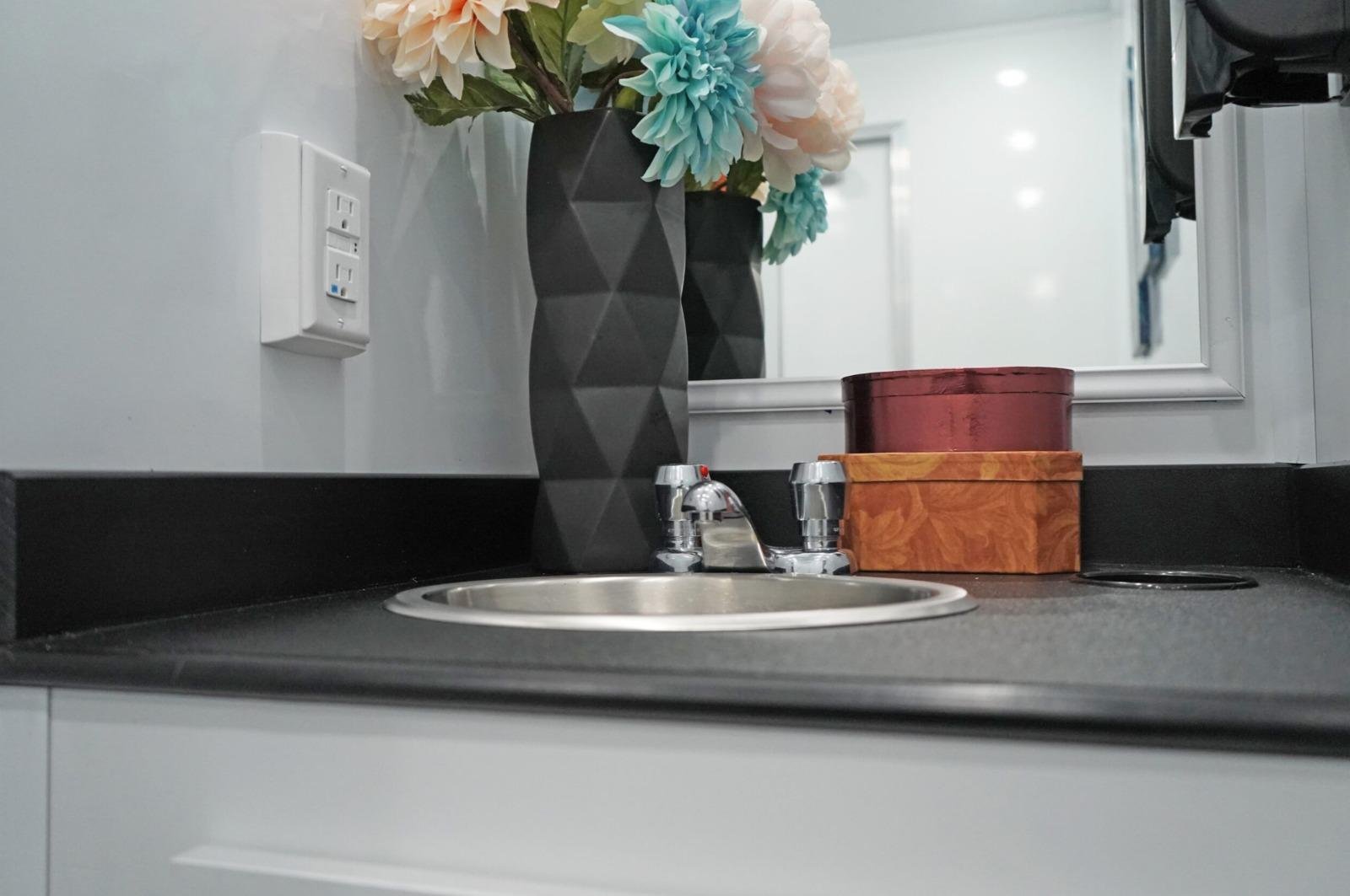 Modern sink and vanity inside a luxury restroom trailer featuring floral decor, mirror, and clean countertop for upscale event experiences.