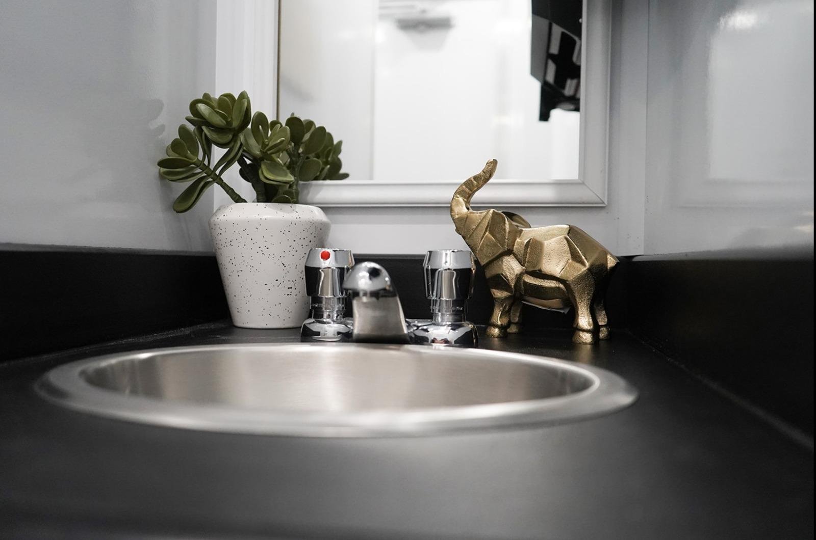 Stylish sink and vanity inside a luxury restroom trailer with decorative plant and gold elephant accent for upscale events.