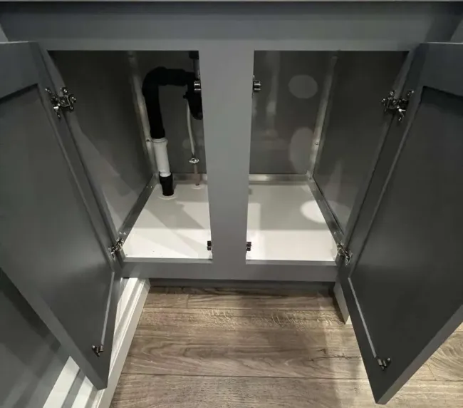 Open vanity cabinet inside a luxury restroom trailer showing plumbing and storage space, available for Colorado event rentals