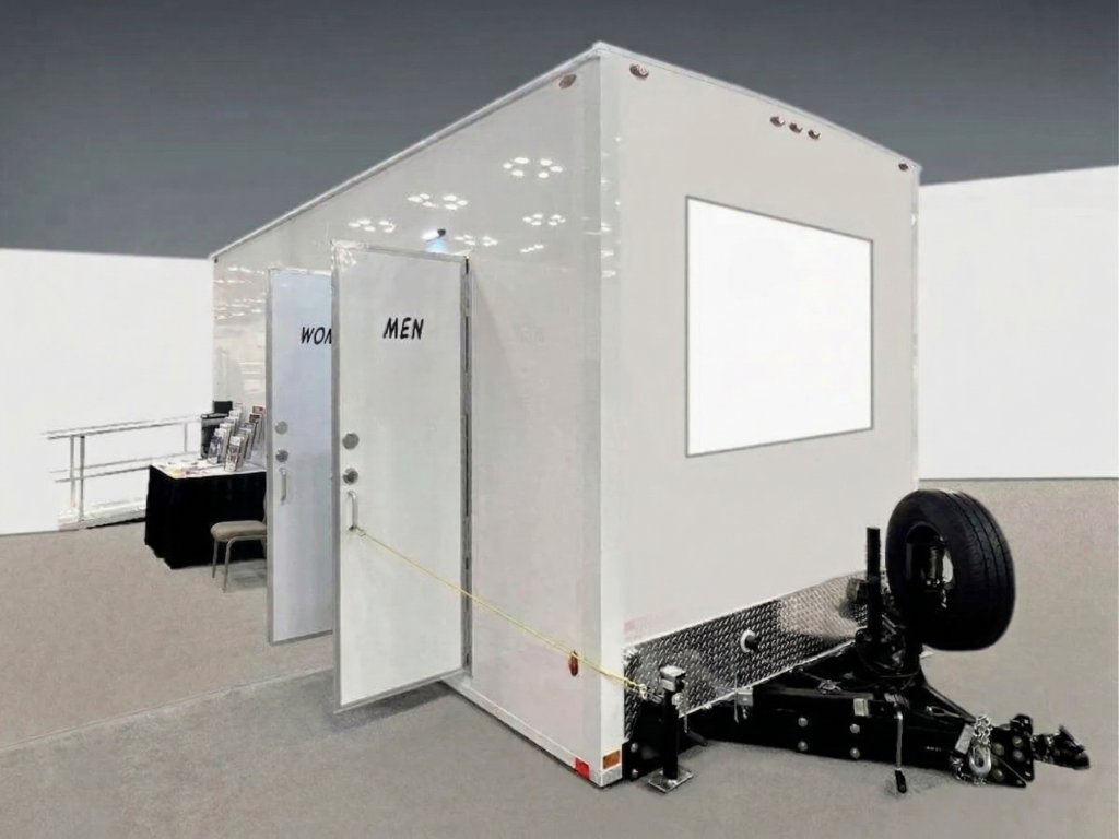 Portable restroom trailer with separate men and women entrances displayed indoors, available for event and construction rentals in Colorado