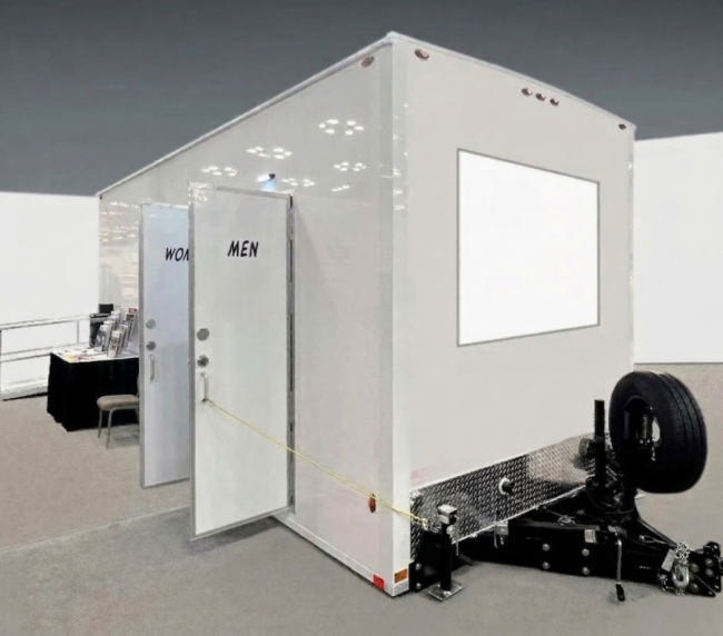 Portable restroom trailer with separate men and women entrances displayed indoors, available for event and construction rentals in Colorado