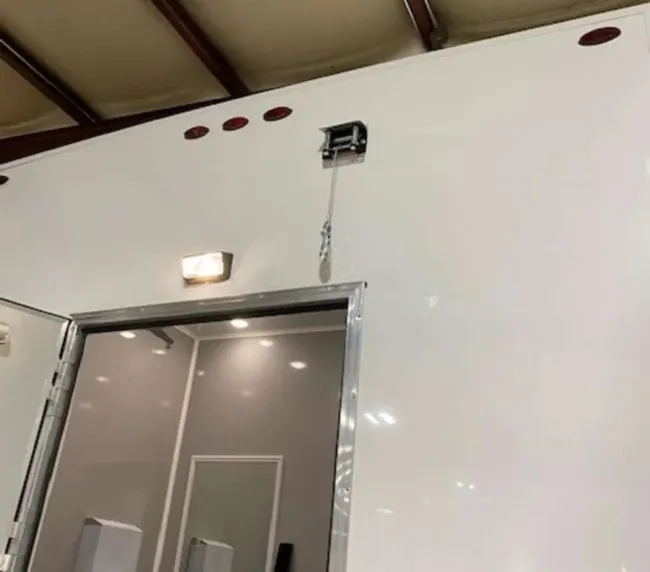 Exterior restroom trailer door with overhead lighting and interior view, suitable for outdoor event rentals in Colorado