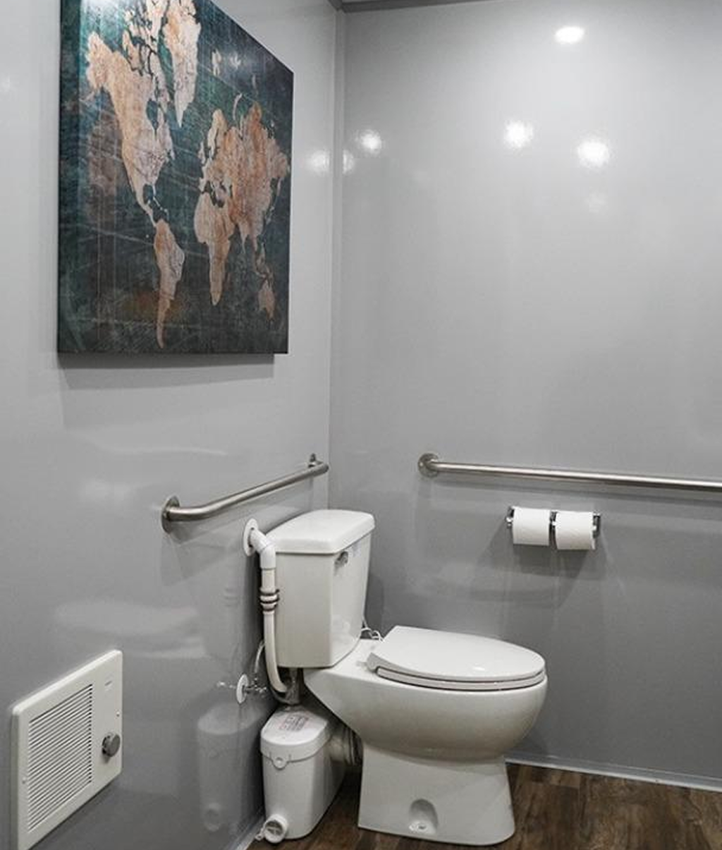 Clean and modern interior of a luxury mobile restroom trailer featuring toilet, grab bars, and elegant decor for event guests.