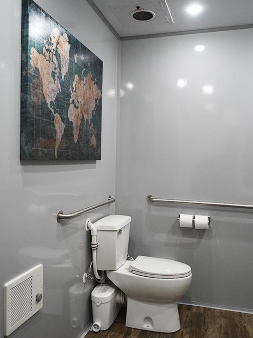 Clean and modern interior of a luxury mobile restroom trailer featuring toilet, grab bars, and elegant decor for event guests.